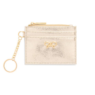 A small metallic gold card holder with a keychain attachment, featuring a bow detail on the front, set against a plain white background.