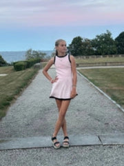 Woman in a pink dress standing on a gravel path with decorative planters and a scenic background.