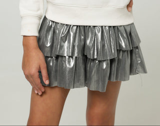 Young girl wearing a white sweater with a decorative design and a silver skirt on a plain background